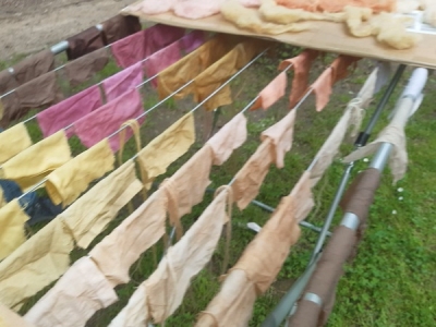 Gefärbte Stoffe in verschiedenen Farben (Braun, Gelb, Beige, Orange und Rosa) hängen auf einem Wäscheständer