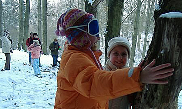 Eine Gruppe Kinder fühlen mit geschlossenen Augen Baumstämme im Winterwald.