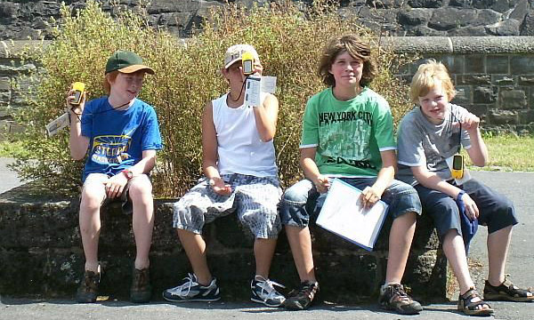 Vier Jugendliche sitzen an der Sperrmauer und halten GPS-Geräte in der Hand.